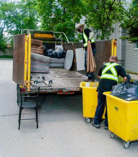 Mr. Garbage junk removal crew loading household furniture and trash bins into a waste disposal truck in Winnipeg.