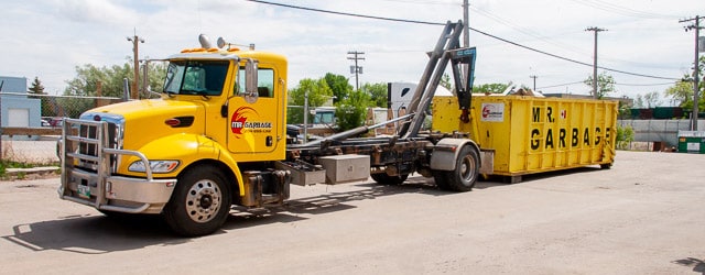 Mr. Garbage truck delivering a large yellow garbage dumpster rental in Winnipeg.