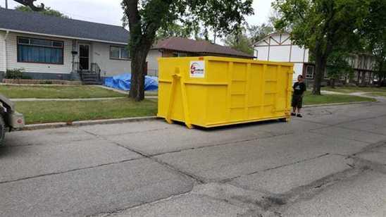 Large yellow garbage bin rental from Mr. Garbage placed on a residential street in Winnipeg for junk removal and debris cleanup.