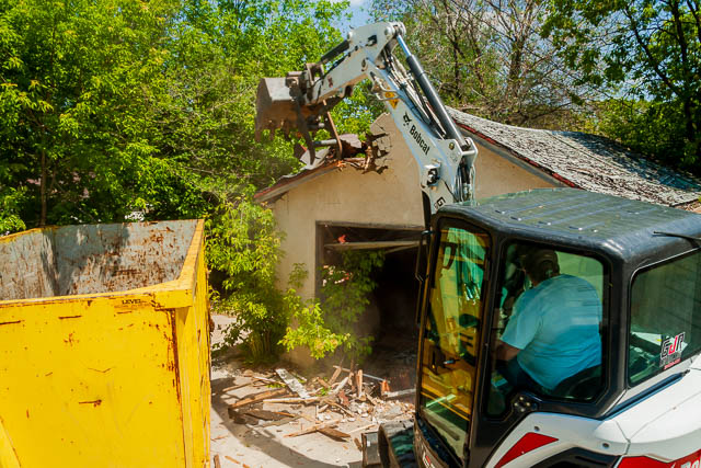 Excavator loading debris into a yellow garbage bin rental in Winnipeg by Mr. Garbage during demolition and junk removal service.
