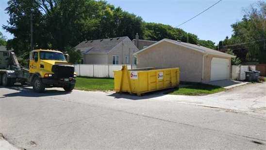 Mr Garbage truck with yellow dumpster beside Winnipeg home – garbage bin rental near me for junk removal, debris disposal, and waste bin rental.
