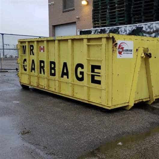 Large yellow Mr. Garbage dumpster rental bin outside commercial building in Winnipeg.