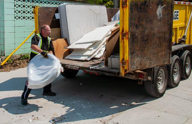 man throwing trash into a large dumpster rental. Dumpster bin reveals to be full of waste