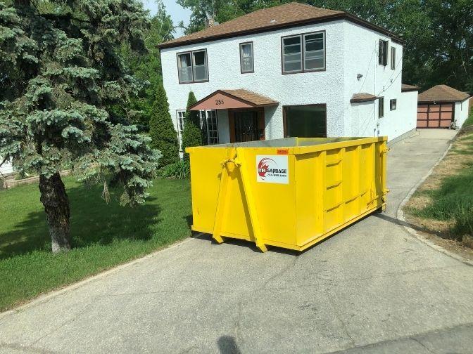 Mr Garbage yellow dumpster rental in Winnipeg driveway – garbage bin rental near me for home renovation cleanup and waste disposal.