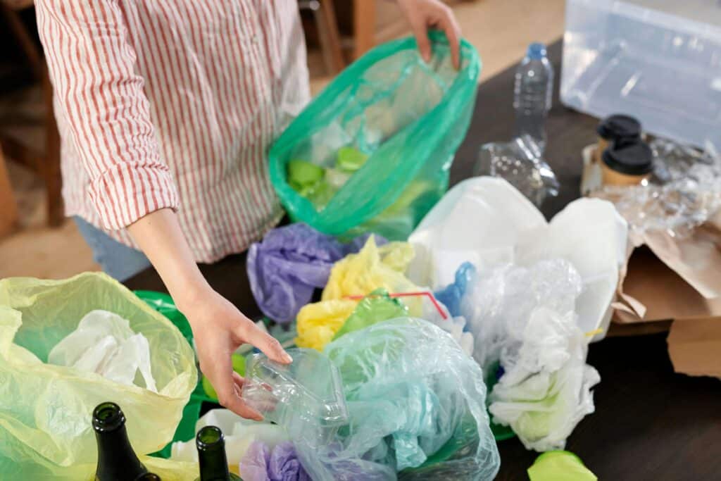 Person sorting plastic waste and bottles into recycling bags for proper garbage disposal