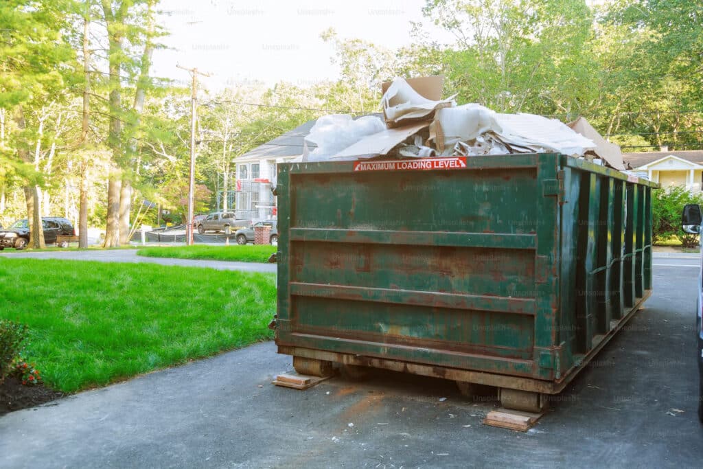 Large green dumpster filled with renovation debris – garbage bin rental Winnipeg for home cleanouts, trash removal, and waste bin rental services.