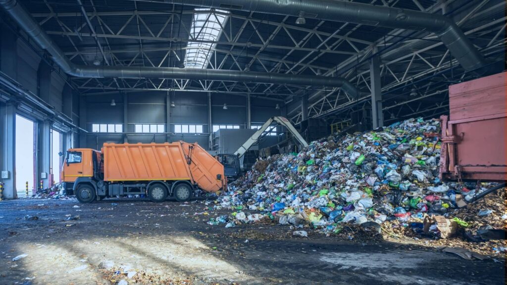 Inside an industrial waste sorting facility with large equipment moving mixed materials on conveyors and workers organizing recyclables for processing.